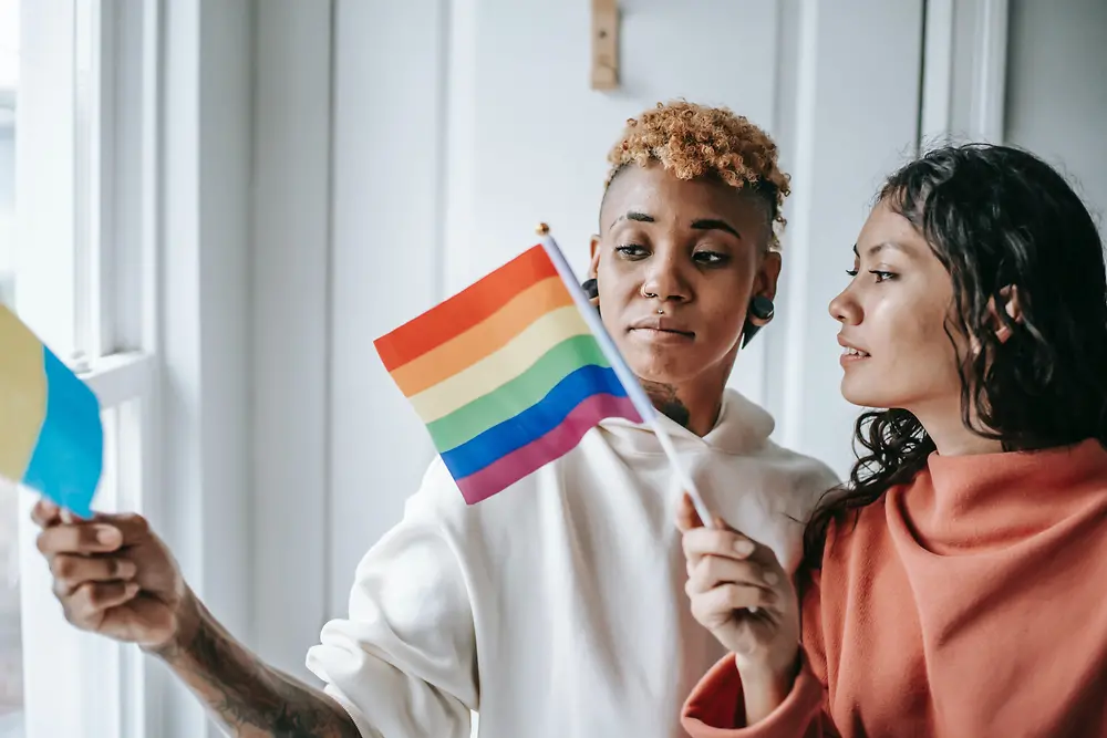 Duas mulheres a conversar enquanto seguram uma bandeira LGBTQ+.