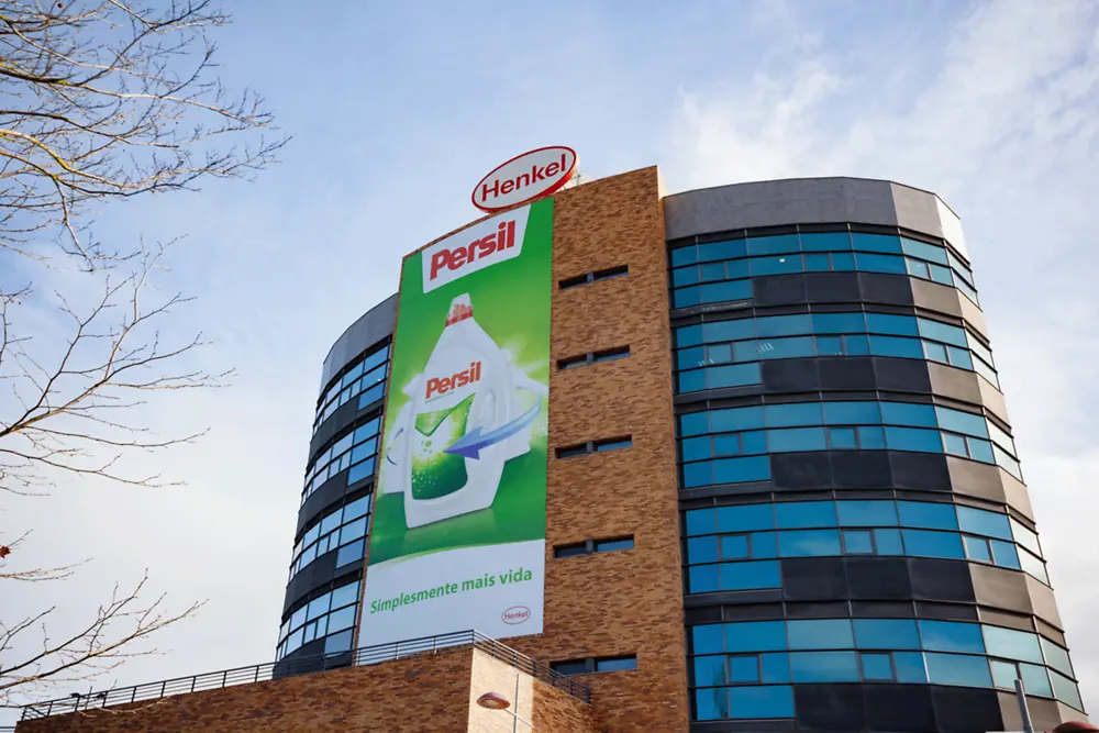 Edifício semicircular da empresa com o logotipo oval da Henkel no telhado e um grande anúncio do Persil na fachada.