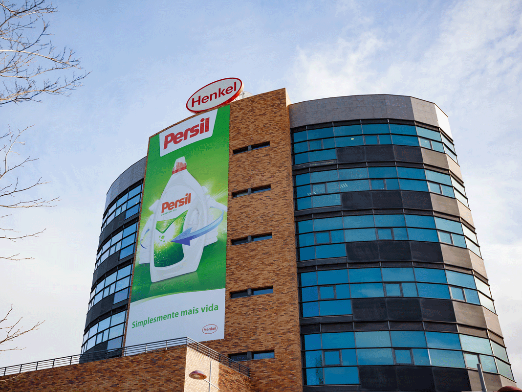 Edifício semicircular da empresa com o logotipo oval da Henkel no telhado e um grande anúncio do Persil na fachada.