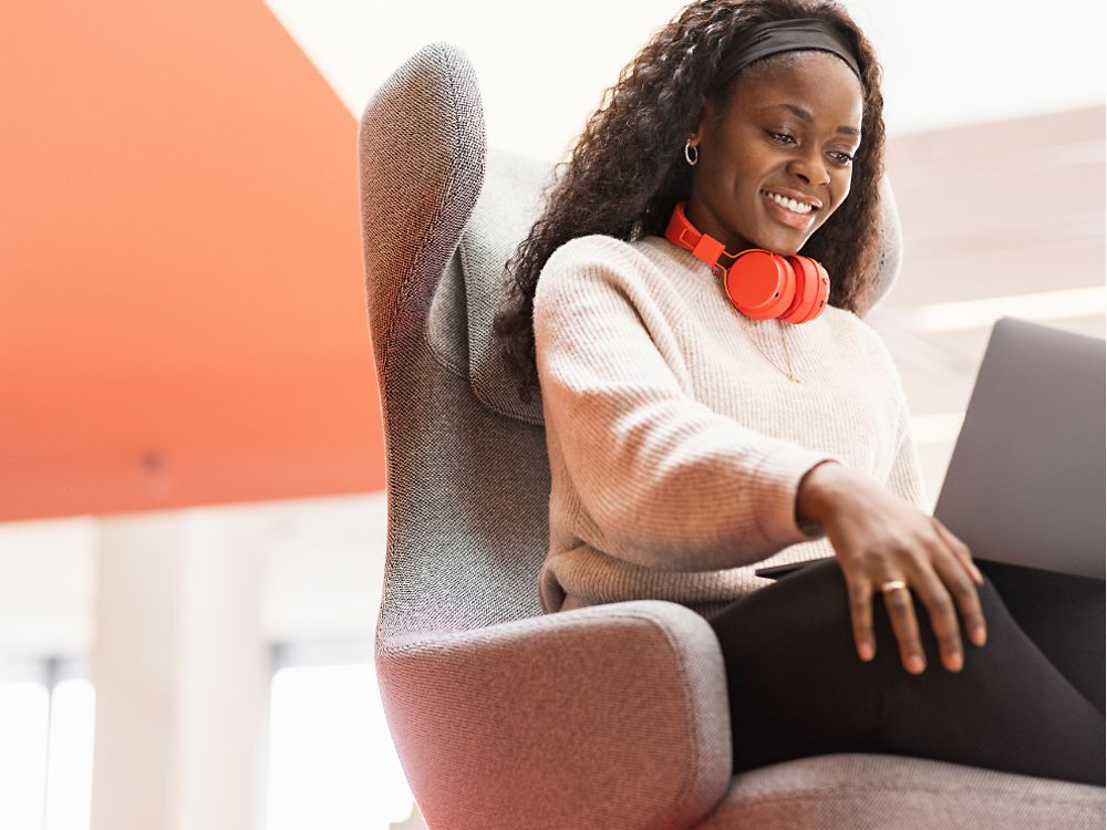 Uma funcionária da Henkel está sentada em uma cadeira confortável com o laptop sobre os joelhos. Ela sorri. 