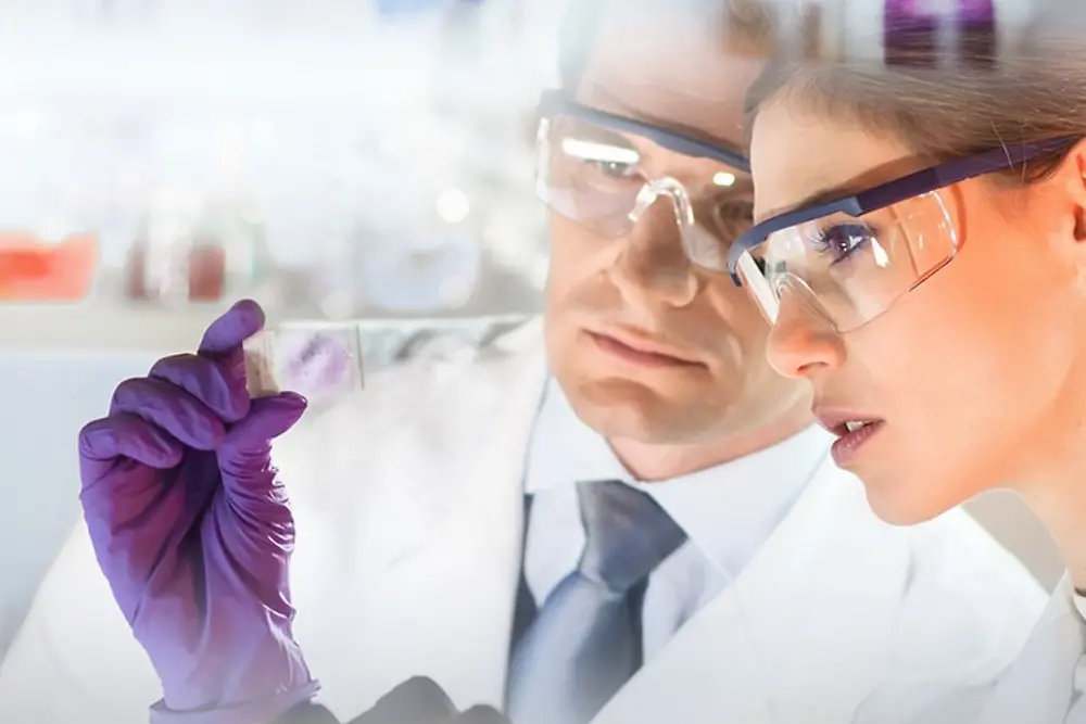 Rostos de uma mulher e de um homem a olhar para uma amostra num laboratório 