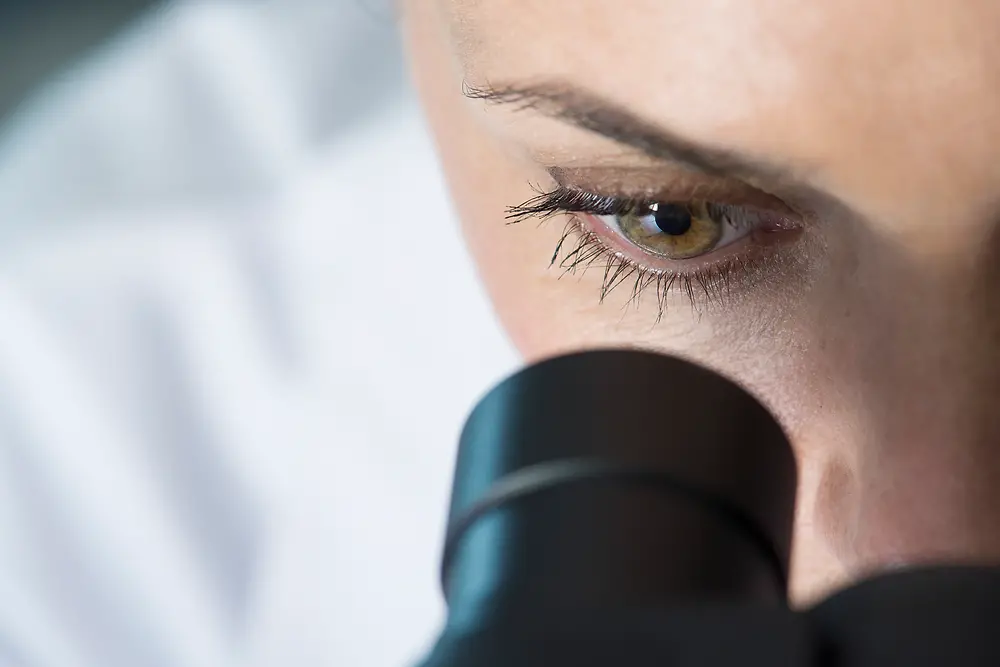 olho de uma mulher a espreitar por um microscópio 