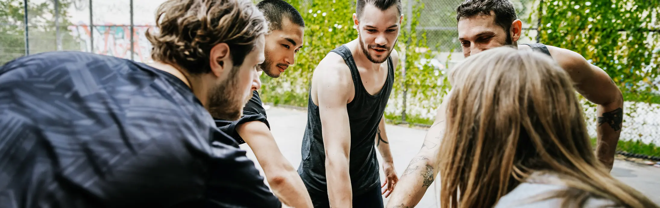 um grupo de diversos jovens em pé em círculo, cada um deles com uma mão no meio