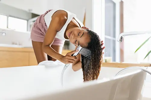 Mulher na casa de banho a lavar os seus longos cabelos castanhos na banheira