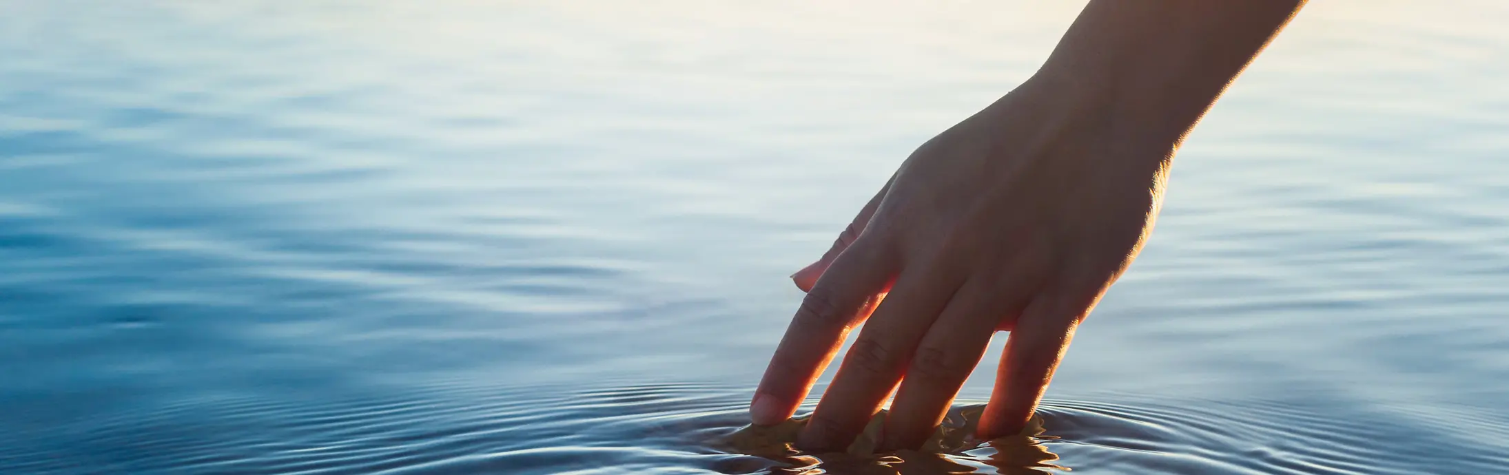 Uma mão passa por uma superfície de água calma com o horizonte de fundo