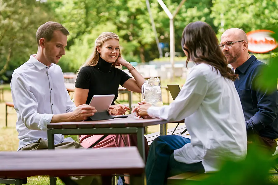 Grupo de colegas sentados juntos ao ar livre, a discutir trabalho com tablets e computadores portáteis, representando a colaboração e uma cultura aberta e orientada para a equipa na Henkel.
