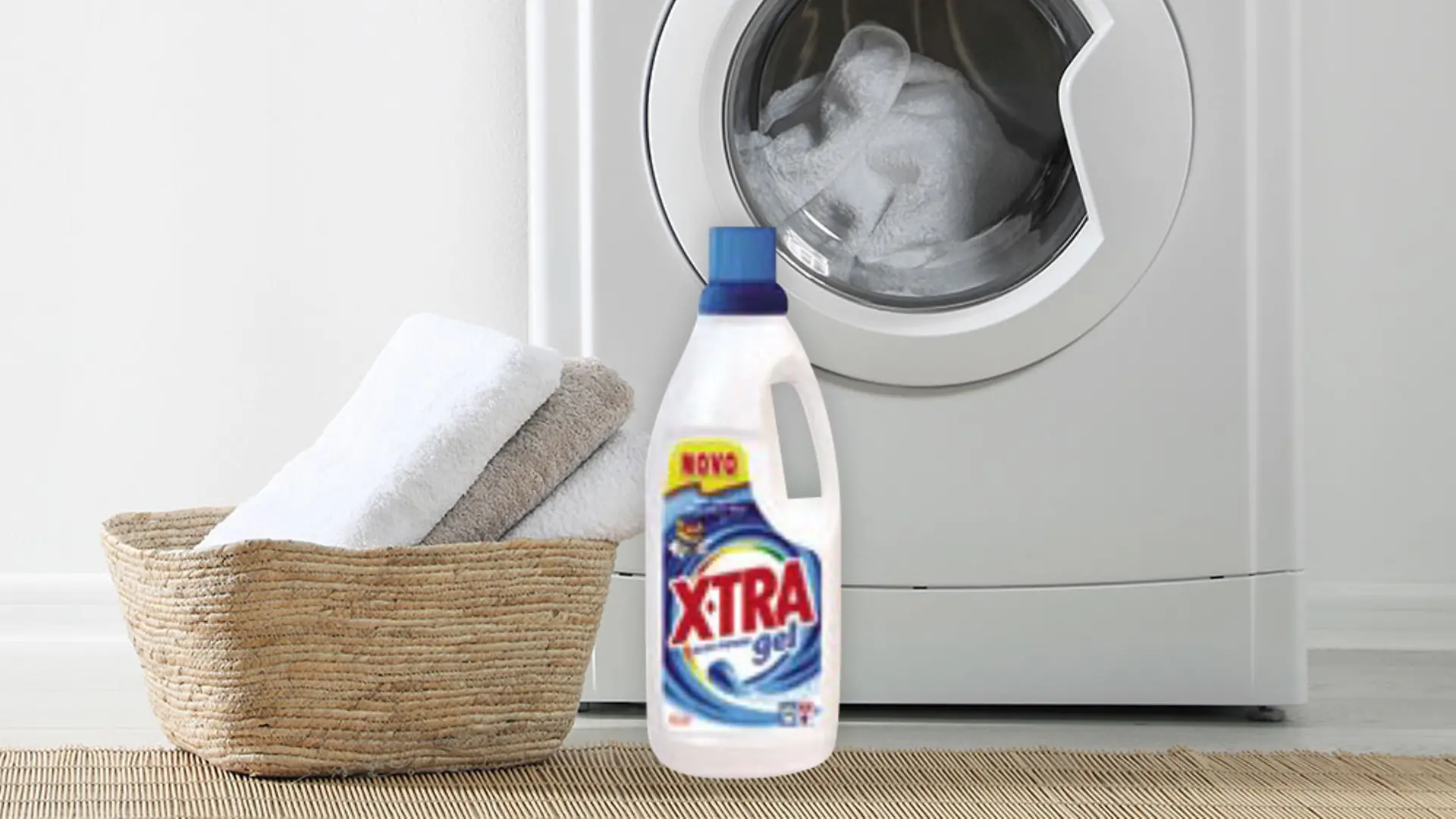 Máquina de lavar roupa com toalhas e detergente X-TRA à frente, marca lançada pela Henkel em Portugal em 2003 para oferecer lavagem inteligente.