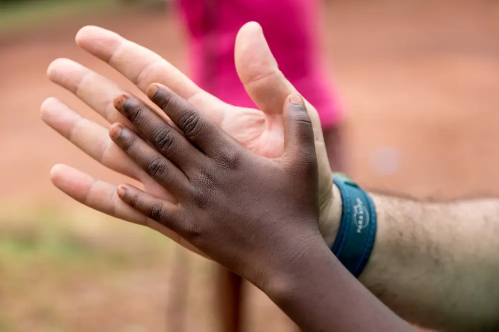 Plano aproximado de duas mãos, uma adulta e outra infantil, apoiadas entre si em sinal de união e colaboração, com fundo desfocado ao ar livre.