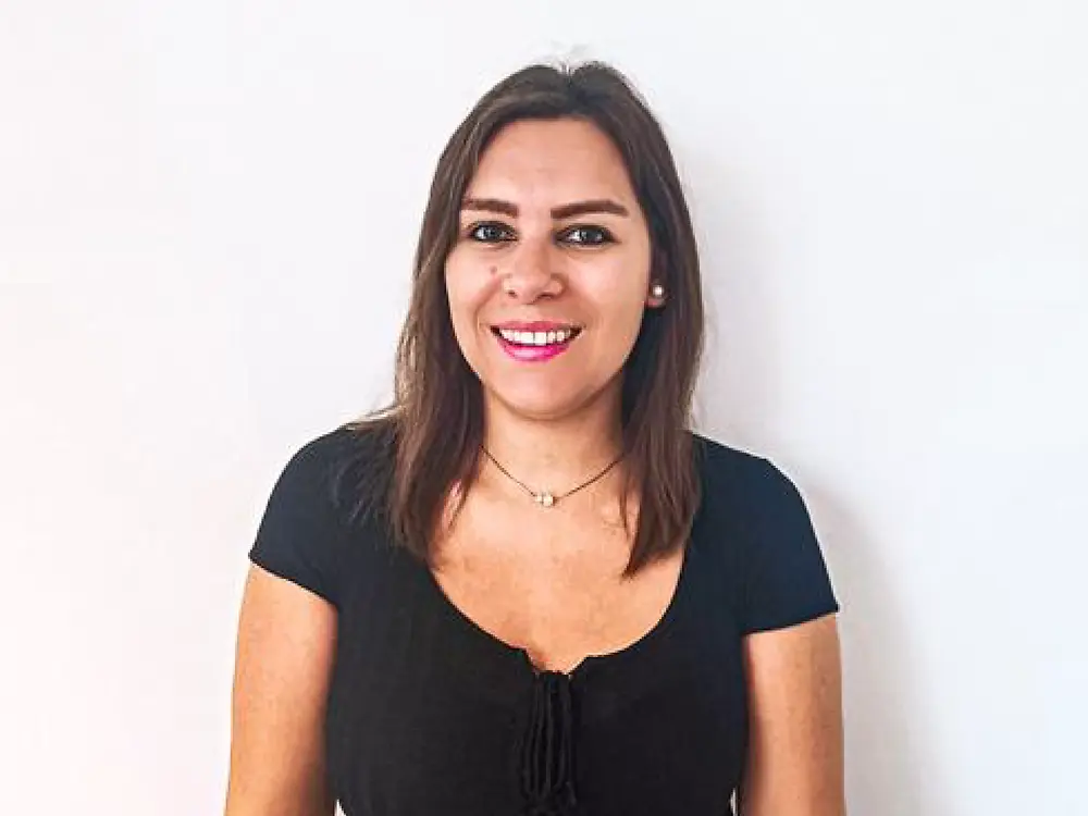 Uma recruitment partner em pé diante de um fundo branco, vestindo uma camisola preta e um cinto bege, a partilhar dicas sobre como lidar com perguntas difíceis em entrevistas.