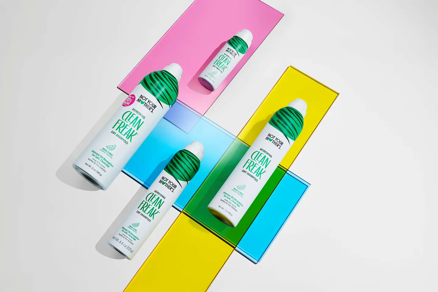 Coleção Clean Freak da Not Your Mother’s com champô seco em vários formatos, apresentada sobre um fundo colorido.