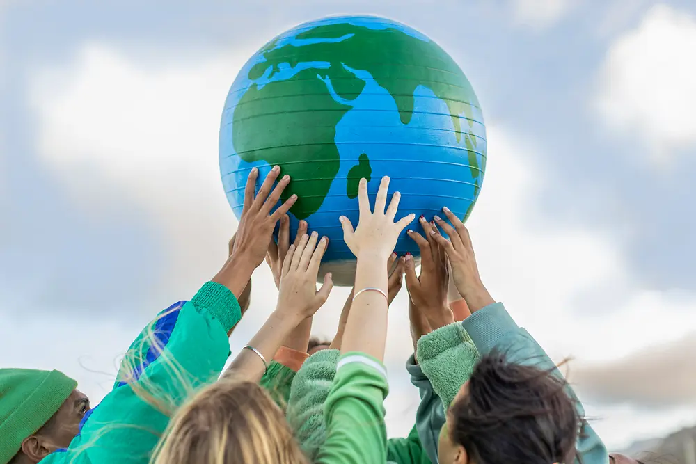 Várias pessoas levantam um globo terrestre azul e verde em direção ao céu, simbolizando os objetivos globais de sustentabilidade e zero emissões líquidas da Henkel para 2045.