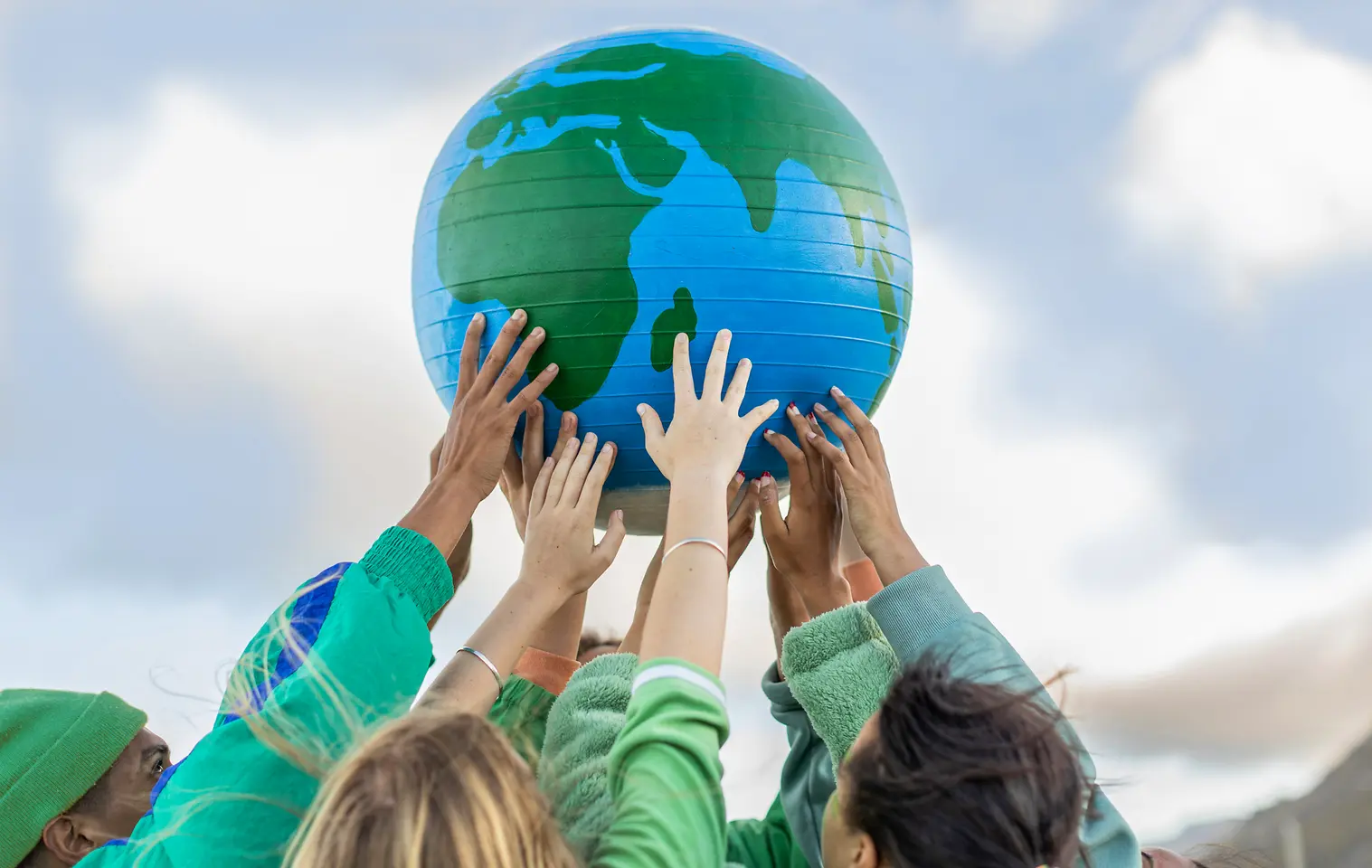 Várias pessoas levantam um globo terrestre azul e verde em direção ao céu, simbolizando os objetivos globais de sustentabilidade e zero emissões líquidas da Henkel para 2045.