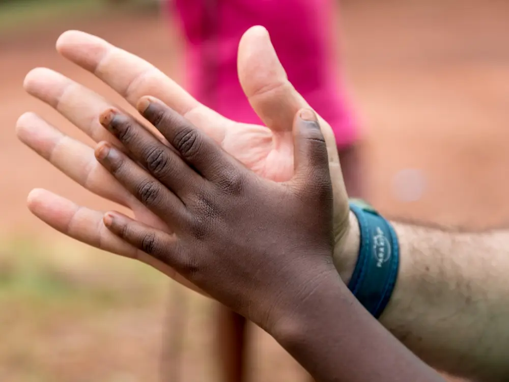 Imagem de uma mão levantada, com uma pulseira azul no pulso, em ambiente exterior, representando simbolicamente a participação em ações de voluntariado do programa MIT da Henkel.