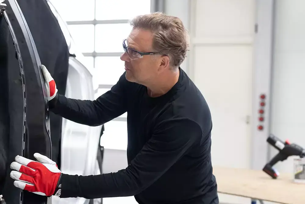 Técnico a reparar ou a fazer a manutenção da porta de um veículo numa oficina mecânica.