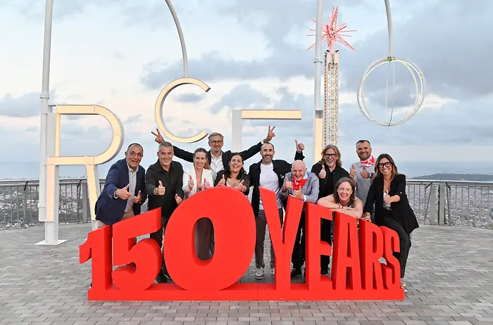 Membros da equipa de direção da Henkel Ibérica posam junto a uma estrutura com a mensagem “150 YEARS” durante o festival comemorativo do 150.º aniversário da Henkel, realizado em Barcelona, com vistas panorâmicas da cidade em segundo plano.