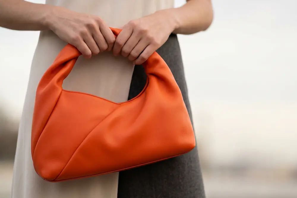 Mala em couro laranja segurada por uma pessoa, exemplo da aplicação das soluções de revestimentos especiais da Stahl para os setores da moda e do luxo.