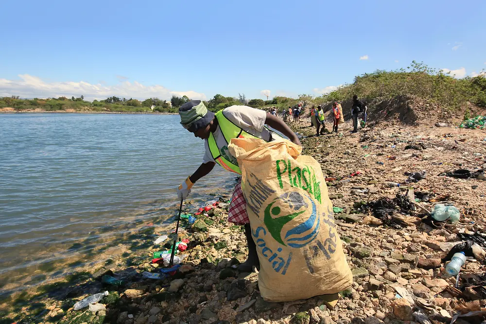 Mulher a recolher resíduos plásticos na praia
