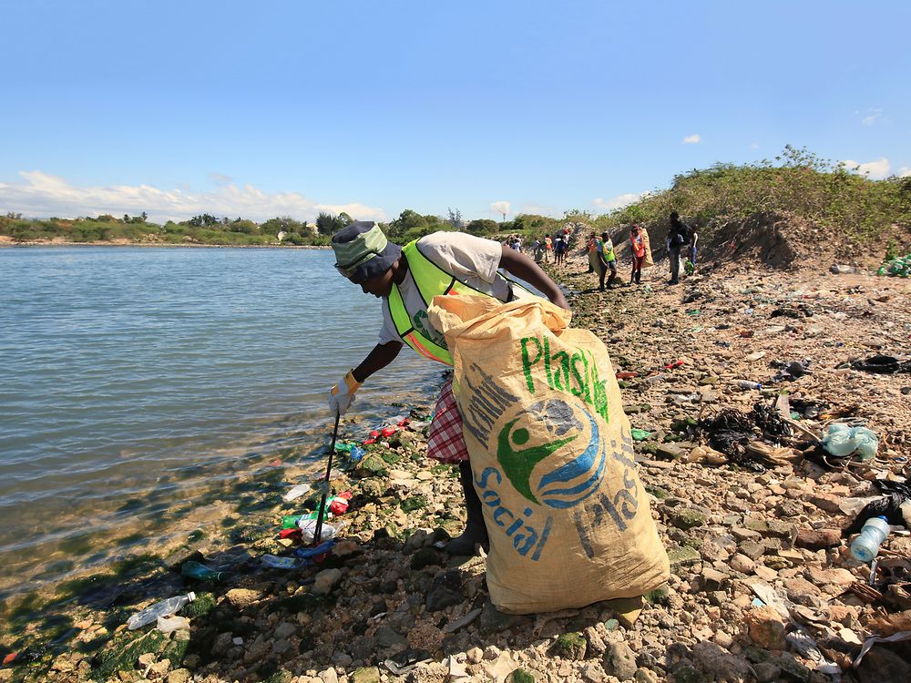 Mulher a recolher resíduos plásticos na praia